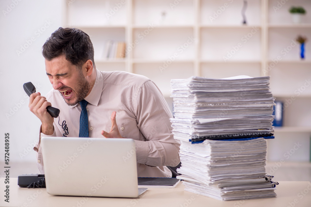 Young male employee unhappy with excessive work in the office Young male employee unhappy with excessive work in the office