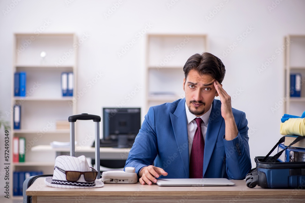 Young male employee preparing for trip at workplace Young male employee preparing for trip at workplace