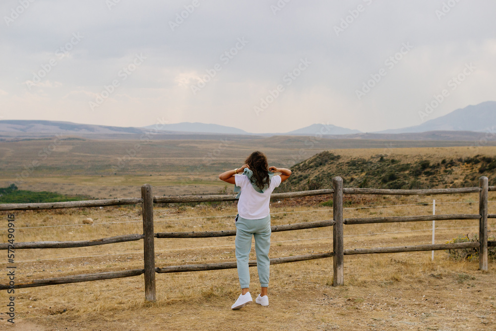 A young brown-haired girl looks into a mountain landscape. Spring panorama with mountains and cloudy sky. Elk Mountain, Wyoming, USA
