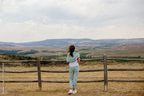 A young brown-haired girl looks into a mountain landscape. Spring panorama with mountains and cloudy sky. Elk Mountain, Wyoming, USA © Liudmila