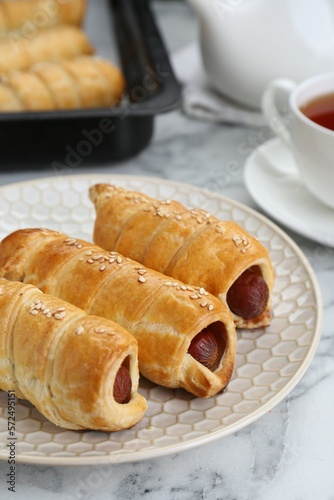 Delicious sausage rolls and hot drink on white marble table  closeup