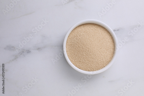 Bowl of active dry yeast on white marble table, top view. Space for text