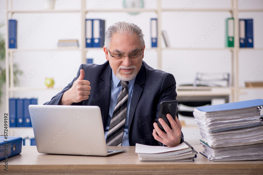 Old male employee speaking by phone in the office Old male employee speaking by phone in the office