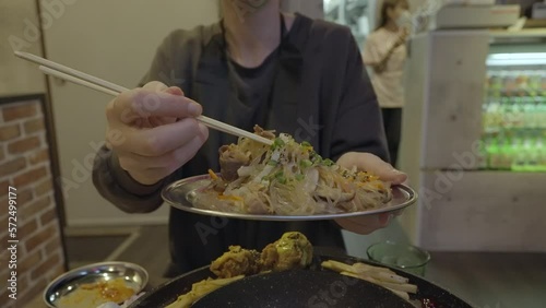 This slow motion video shows anonymous hands holding a Korean japchae noodle dish and grabbing large bites with chopsticks.