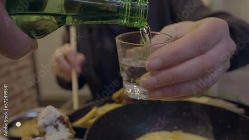 This POV video shows a soju sake bottle pouring alcohol into a shot glass in slow motion.
