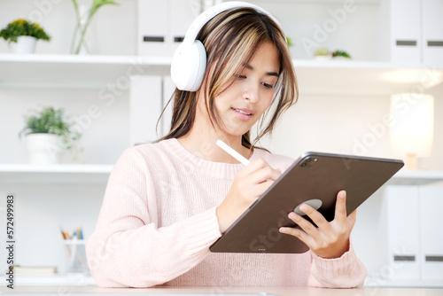 Happy young asian woman with headphones using digital tablet at home