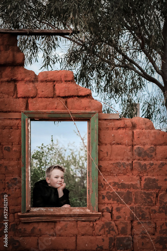 Young boy looking out window of destroyed mud brick house on remote property © Caseyjadew