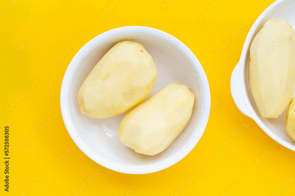 Raw peeled potatoes in white plate on yellow background.