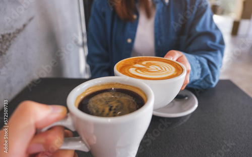 Closeup image of a couple people clinking coffee cups together in cafe