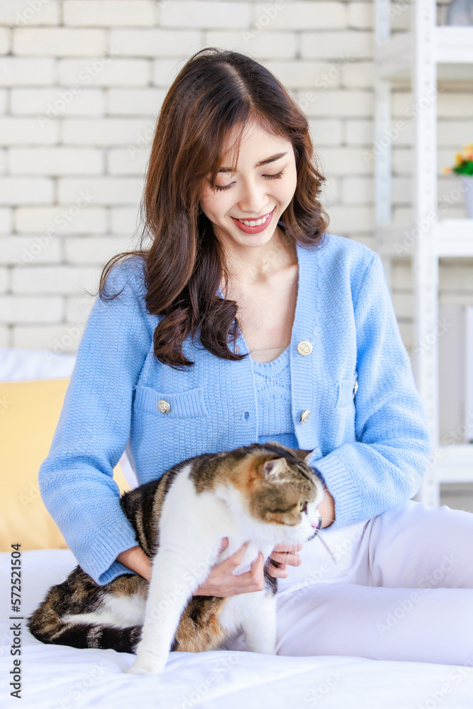 Millennial Asian young kindly cheerful female owner sitting on bed holding hugging cuddling showing love with short hair cute little domestic kitten furry pussycat pet friend on blanket Millennial Asian young kindly cheerful female owner sitting on bed holding hugging cuddling showing love with short hair cute little domestic kitten furry pussycat pet friend on blanket