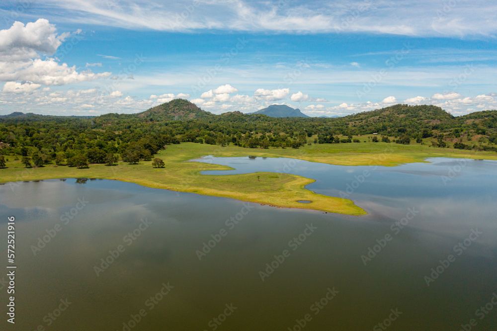 Top view of valley with a lake and tropical vegetation against a blue sky and clouds. Sorabora lake, Sri Lanka.