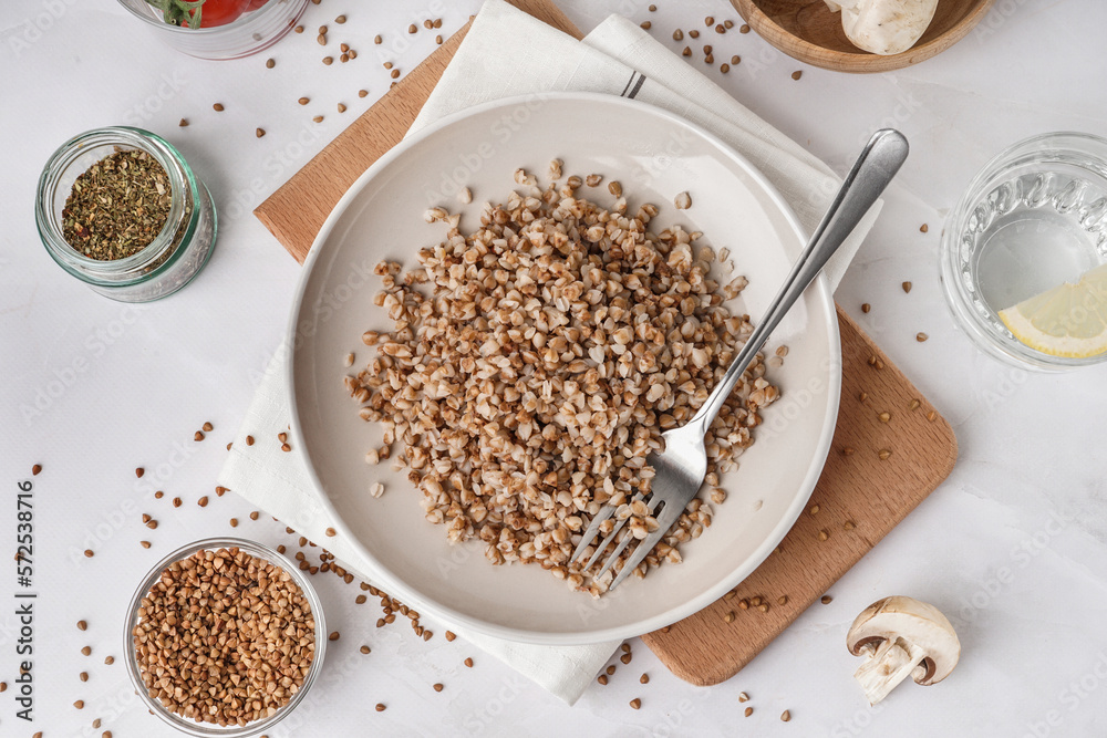 Board with plate of tasty buckwheat porridge on white table Board with plate of tasty buckwheat porridge on white table