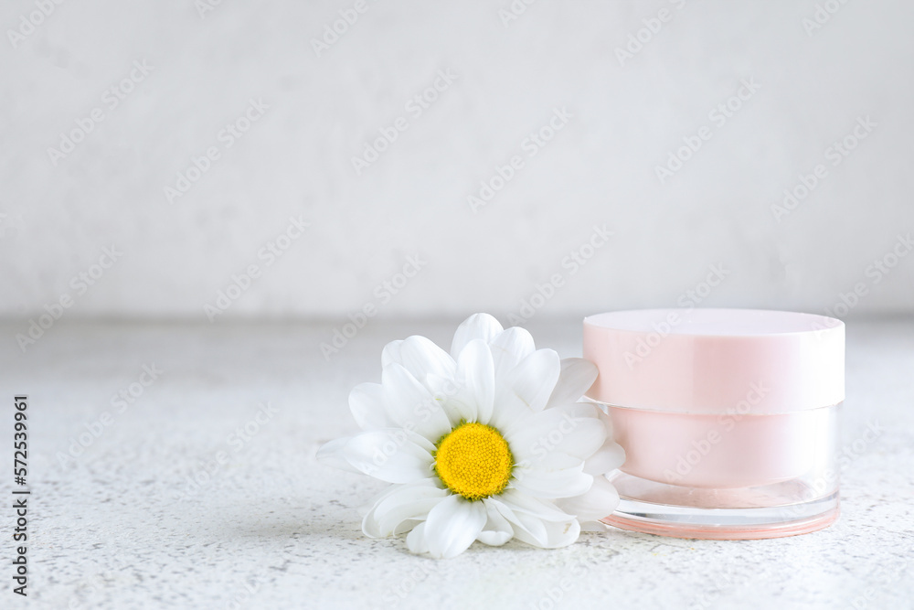 Jar of cosmetic product and chamomile flower on light background