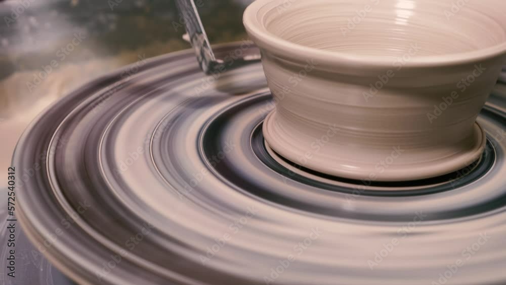 A potter using a special tool to remove excess clay from the finished product on the potter's