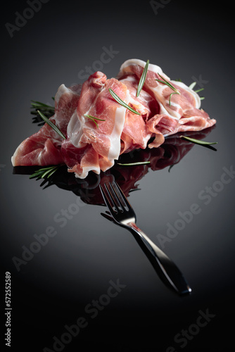 Italian prosciutto or Spanish jamon with rosemary on a black background.