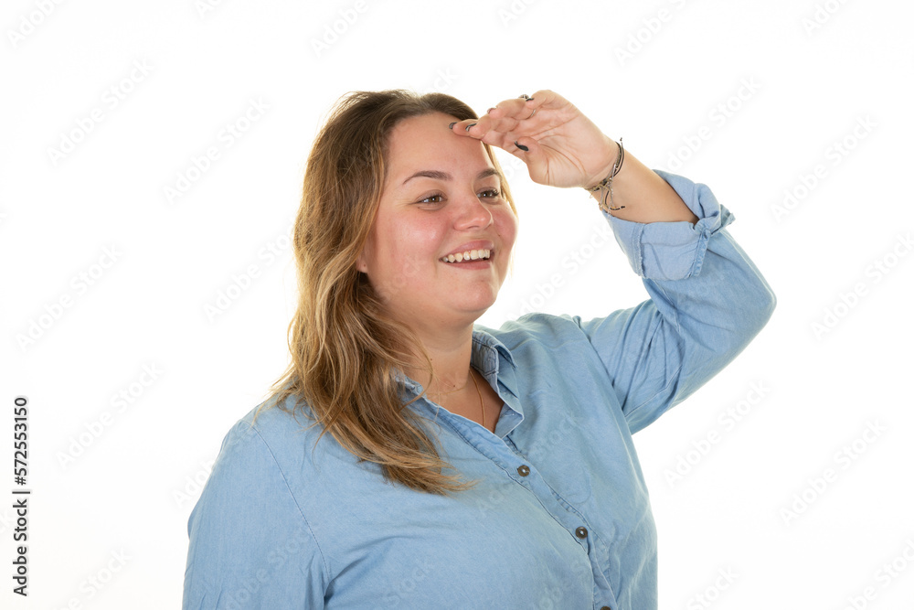 Smiling happy woman looking far away with hand cap over forehead beautiful blonde plus size body positive girl on white wall background in studio portrait Smiling happy woman looking far away with hand cap over forehead beautiful blonde plus size body positive girl on white wall background in studio portrait