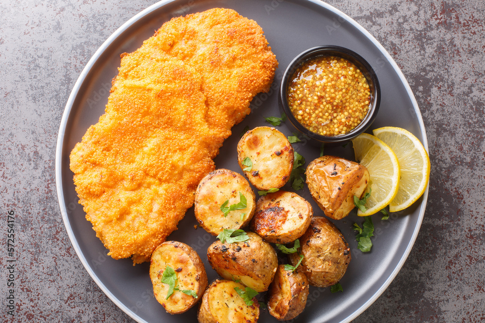 Delicious German Munich schnitzel fried breaded with mustard and horseradish served with baked potatoes close-up in a plate on the table. horizontal top view from above