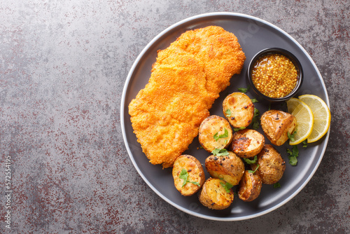 Obraz na płótnie Homemade Munich veal schnitzel fried in breadcrumbs with mustard and horseradish garnished with baked potatoes close-up in a plate on the table. horizontal top view from above w salonie