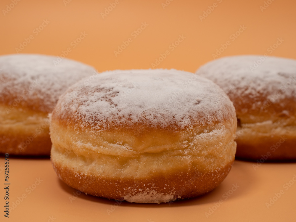 Freshly baked and dusted with powdered sugar German donuts. Donut berliner or krapfen on orange background.