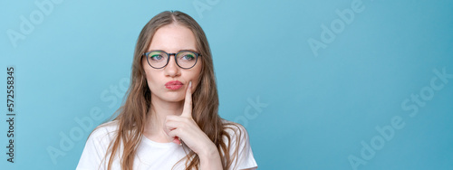 Worried stupid and insecure young woman with long hair nervous fingers in alarm and panic, frowning with a worried expression in a white t-shirt on a blue background in the studio