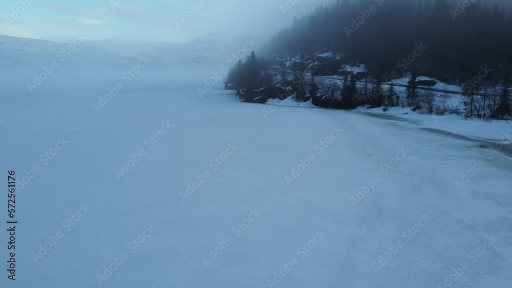 flying over frozen lake with ice fog in the forest and over the lake with snowy mountain backdrop flying over frozen lake with ice fog in the forest and over the lake with snowy mountain backdrop
