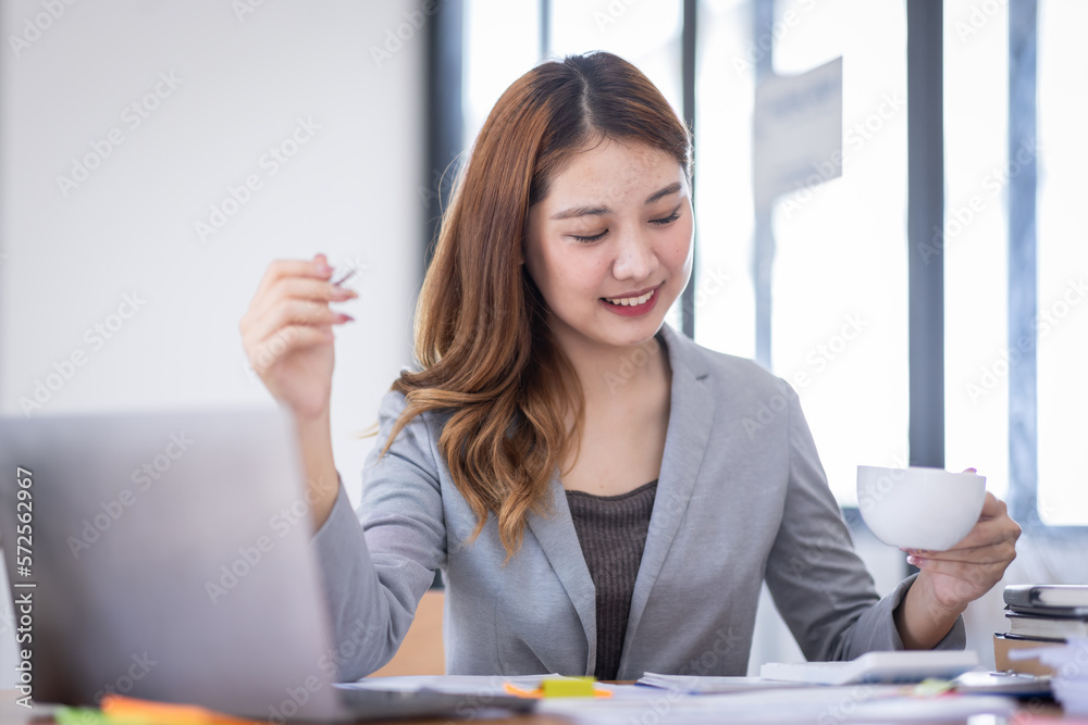 Business Asian woman using calculator and writing make note with calculate doing math finance on an office desk. Woman working at office with laptop and tax, accounting, documents on desk. Business Asian woman using calculator and writing make note with calculate doing math finance on an office desk. Woman working at office with laptop and tax, accounting, documents on desk.
