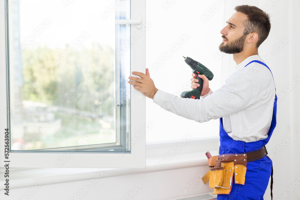 handsome young man installing bay window in a new house construction site. handsome young man installing bay window in a new house construction site.