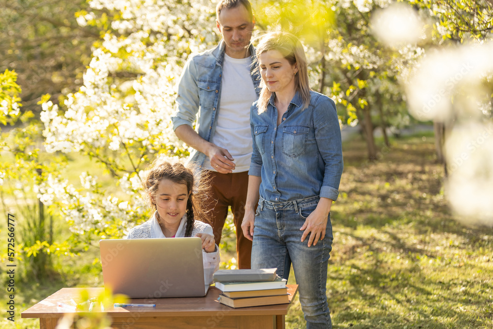 Happy family of four parents and cute little girl studying on laptop, enjoy using laptop watching cartoons, make internet video call or shopping online looking at computer screen sit together outdoor Happy family of four parents and cute little girl studying on laptop, enjoy using laptop watching cartoons, make internet video call or shopping online looking at computer screen sit together outdoor