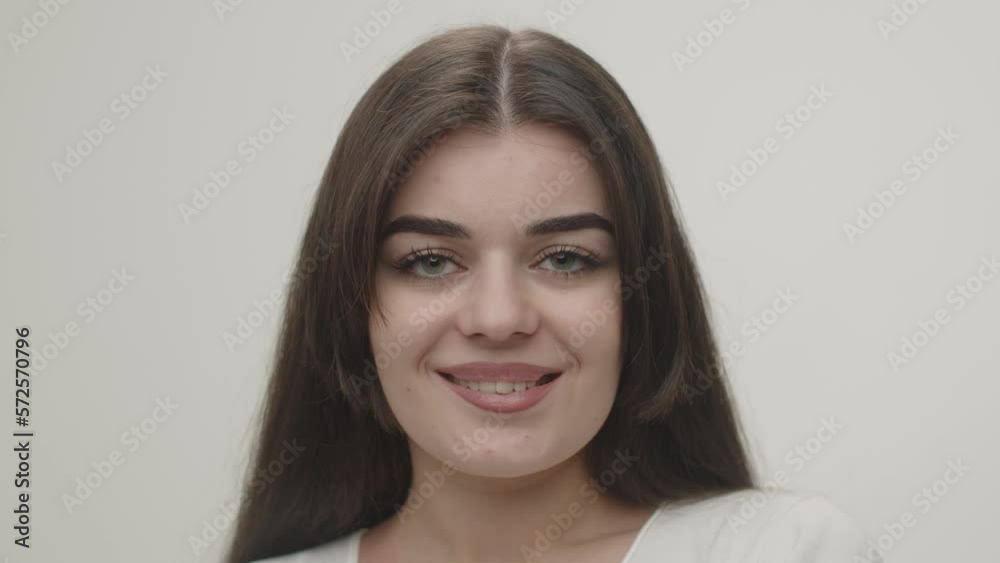 A young brunette woman smiles sweetly and looks intently into the camera. Studio shot of a beautiful brunette on a white background. A young brunette woman smiles sweetly and looks intently into the camera. Studio shot of a beautiful brunette on a white background.