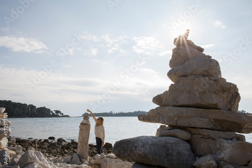 Woman balances rock on top of balancing rocks by sea