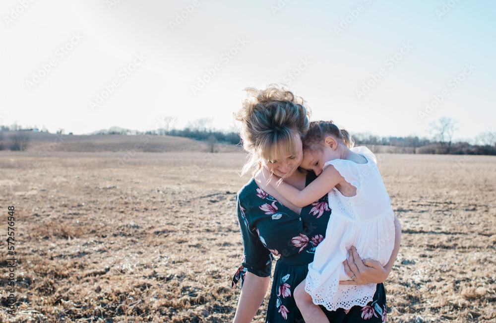 mother holding her daughter whilst walking through a field at sunset