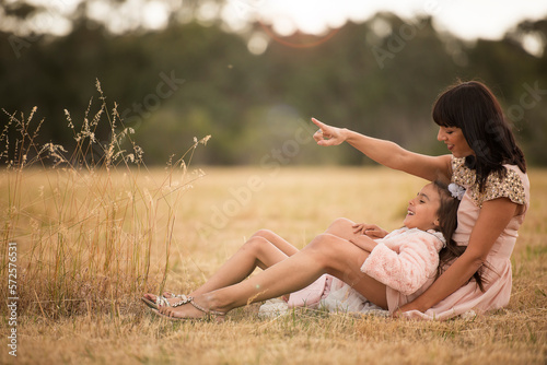 mother showing daughter something sitting on ground in field in nature