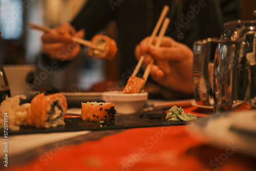 The man and woman in the background eating sushi цшер chopsticks
