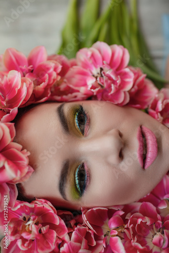 The face of beautiful woman with colorful make-up and flowers . The attractive woman lies in tulips.