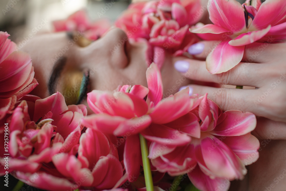 Portrait of a girl with good skin,perfume and cosmetics conceptThe face of beautiful woman with colorful make-up and flowers . The attractive woman lies in tulips. Portrait of a girl with good skin,perfume and cosmetics conceptThe face of beautiful woman with colorful make-up and flowers . The attractive woman lies in tulips.