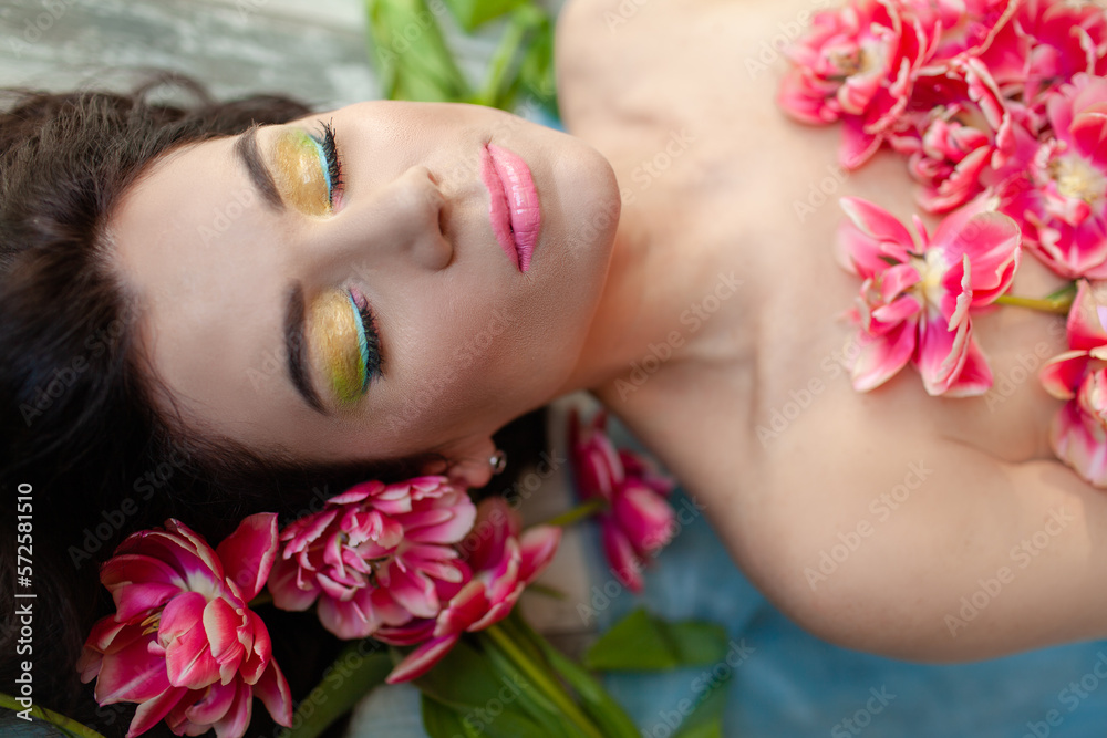 Portrait of a girl with good skin,perfume and cosmetics conceptThe face of beautiful woman with colorful make-up and flowers . The attractive woman lies in tulips. Portrait of a girl with good skin,perfume and cosmetics conceptThe face of beautiful woman with colorful make-up and flowers . The attractive woman lies in tulips.