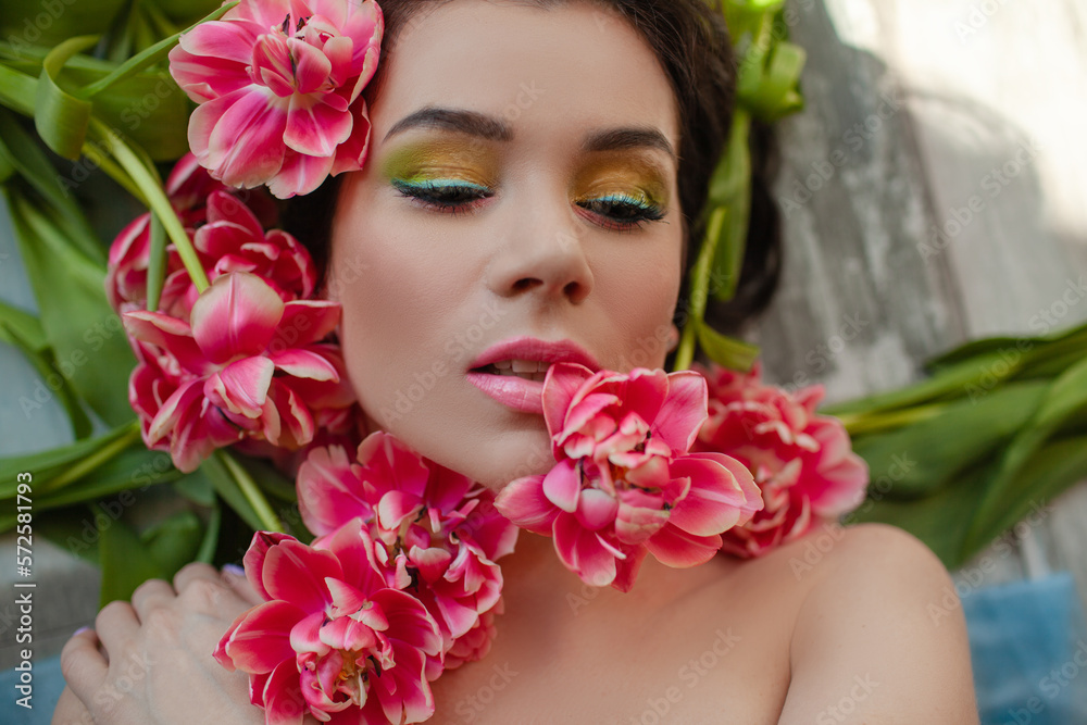 Portrait of a girl with good skin,perfume and cosmetics conceptThe face of beautiful woman with colorful make-up and flowers . The attractive woman lies in tulips. Portrait of a girl with good skin,perfume and cosmetics conceptThe face of beautiful woman with colorful make-up and flowers . The attractive woman lies in tulips.