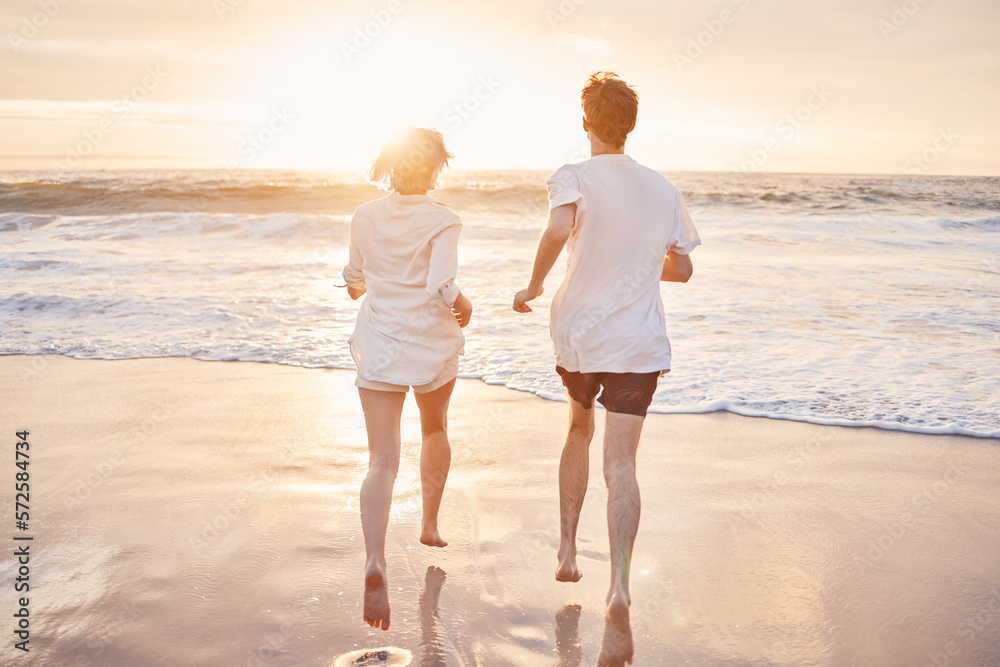 Couple at beach, running to ocean with travel and freedom outdoor, love and care in relationship with youth. Care free at sunset, nature and sea waves with young people back view on holiday in Hawaii Couple at beach, running to ocean with travel and freedom outdoor, love and care in relationship with youth. Care free at sunset, nature and sea waves with young people back view on holiday in Hawaii
