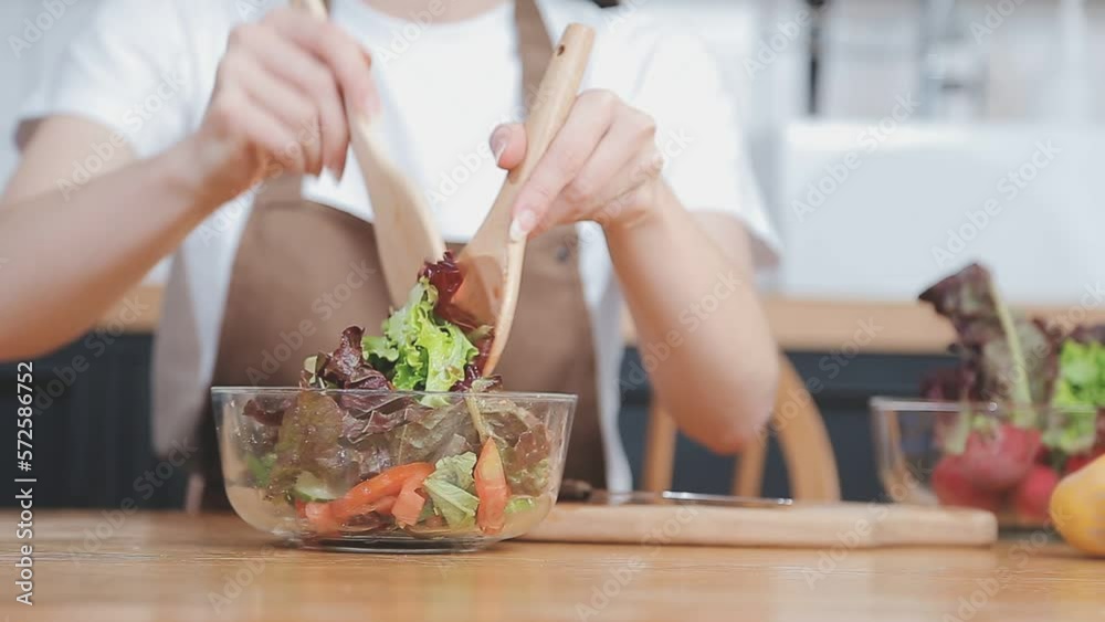 Young and happy woman eating healthy salad sitting on the table with green fresh ingredients indoors Young and happy woman eating healthy salad sitting on the table with green fresh ingredients indoors