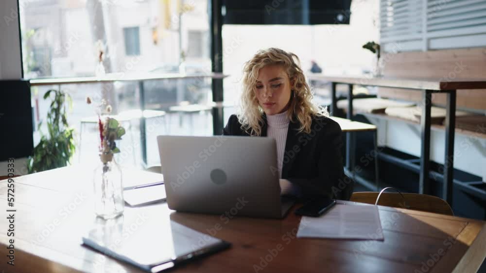 Concentrated female using laptop computer while sitting in urban cafe. Young attractive woman administrator keeps records in electronic form and solves the work tasks of coffee shop. Slow motion Concentrated female using laptop computer while sitting in urban cafe. Young attractive woman administrator keeps records in electronic form and solves the work tasks of coffee shop. Slow motion