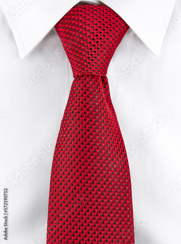 Close-up of a necktie made of red silk with a geometric pattern, tied with a Windsor knot on a white shirt with a classic collar. Vertical image.