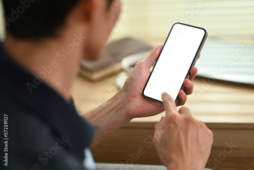Young man hand checking social media on mobile phone. Over shoulder closeup view, blank screen for graphic display montage