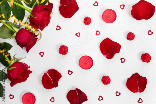 Composition of red roses, rose petals, sequin hearts, candles, gold ribbons on white background. Content for Birthday, Valentines Day, Womens day, Mothers day. Flat lay, top view, close up