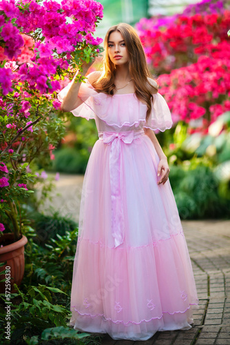 Beautiful girl in pink vintage dress and straw hat standing in garden near colorful flowers. Art work of romantic woman .Pretty tenderness model looking at camera.
