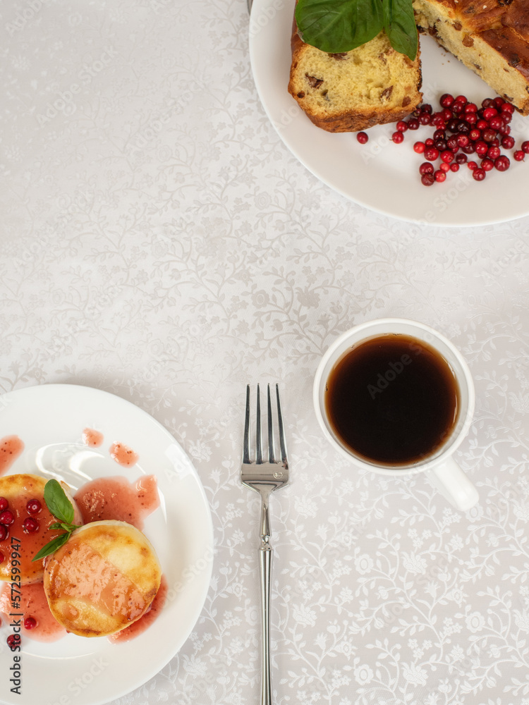 Breakfast on table with light fabric tablecloth. Cheesecakes in Berry syrup with tea and cake. Food photo flat lay