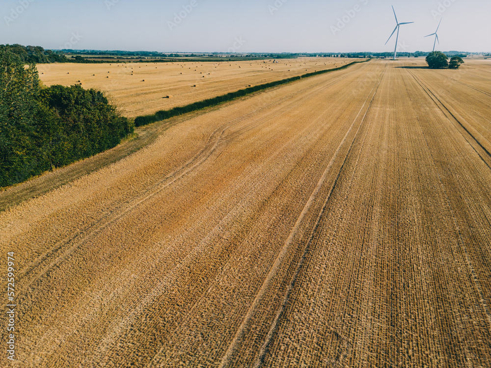 Freshly harvested golden farmer's fields with hay bales and wind turbines in the distance.