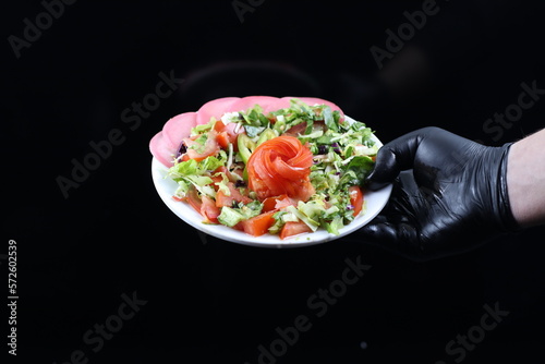 Hand Holding Salad Serving Plate Garnished with Flower-Shaped Tomato Slices - Isolated on Black Background