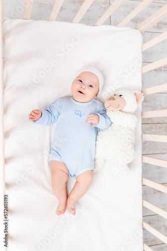 baby in crib with teddy bear toy goes to bed or woke up in the morning, family and birth concept