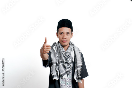 Religious muslim asian man wearing turban, muslim dress and cap, showing thumbs up that he agrees. Isolated on white background.