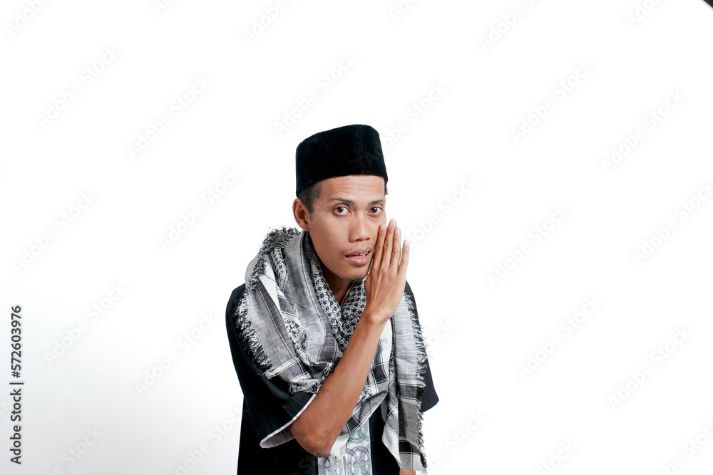 Religious muslim asian man wearing turban, muslim dress and cap. While giving info in a whisper, hands near mouth. isolated on white background.